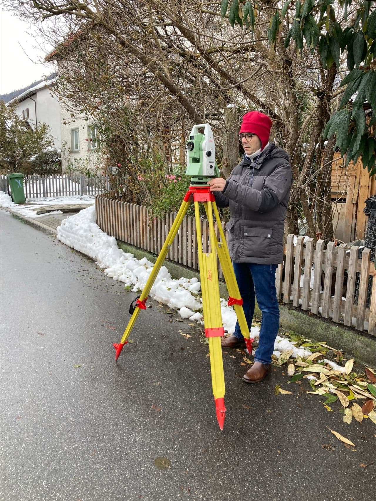 Person bedient ein Vermessungsgerät auf einem Stativ im Winter.