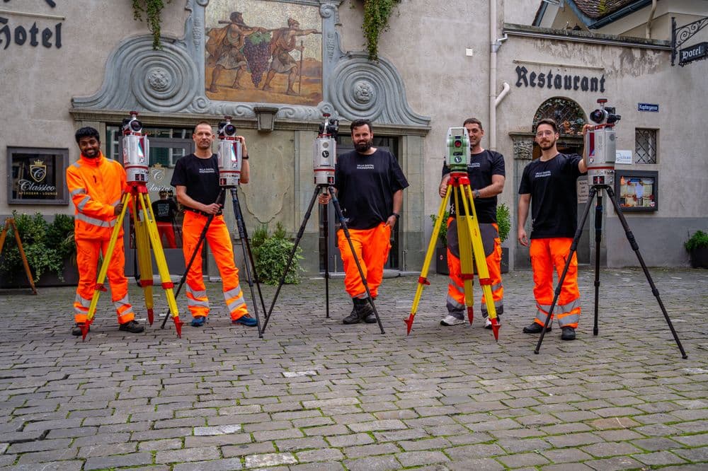 Vermessungsteam mit Theodoliten vor einem Hotel und Restaurant.