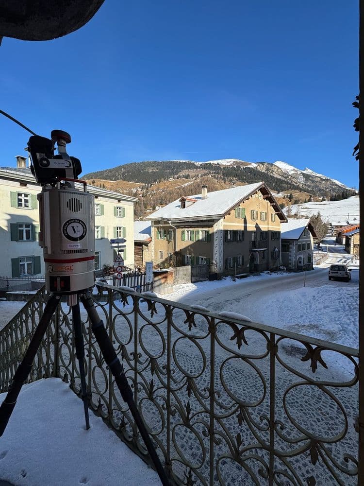 Lasermessgerät auf Balkon mit schneebedecktem Dorf und Berg im Hintergrund.