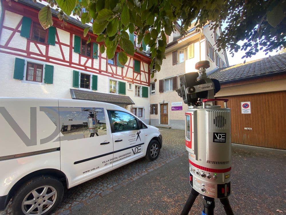 Vermessungsausrüstung vor historischem Gebäude in der Altstadt, weißer Firmenwagen daneben.